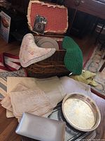 Wicker picnic basket with open lid lined in red and white gingham fabric, partially visible ceramic plates and linens around basket, silverplated trays in front.
