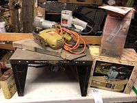 Craftsman router table with yellow router mounted, orange cord, metal stand, boxes and tools visible.