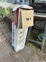 Box of roofing underlayment placed next to outdoor furniture on a brick surface, showing the side with product details and slight wear on box.