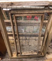 Front view of three weathered wooden framed wire mesh screens stacked together showing wire mesh and aged wood frame.