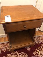 Front view of wooden side table with single drawer and open bottom shelf on patterned rug.