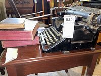 Antique Woodstock typewriter on wood table next to stacked vintage books