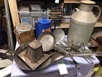 Vintage metal kitchen utensils, fry pan, grater, coffee percolator, and milk jug arranged on a table.