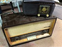 Two vintage radios stacked, Zenith on top and Grundig below, showing front view with dials, buttons, and speaker grille