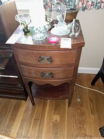 Front view of vintage mahogany side table, showing two drawers with brass pulls and lower shelf on wood floor.