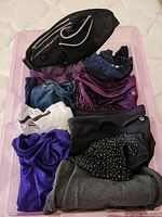 Plastic bin containing folded XL size activewear including T-shirts, yoga pants and a black and white fanny pack.