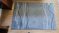 Top down view of entire gray area rug showing wave line pattern on light wood floor.