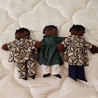 Photo of the set of three artisan dolls lying on a quilted surface, showing each doll's outfit and hair details.