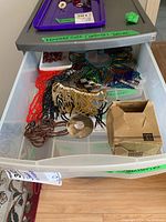 One drawer containing multiple fashion accessories including beaded necklaces, cardboard box, and other jewelry items.