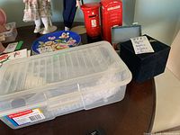 Wide view of lot showing plastic containers, blue floral decor plate, and labeled boxes with decor balls and bells.