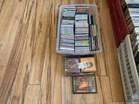 Full top-down view of plastic box filled with CDs along with a few loose CDs outside the box on the wood floor