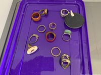 Top view of all eleven rings displayed on a purple plastic surface to show the lot contents and variety of styles and materials.