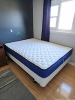 Angled corner view of the mattress and box spring setup in a room corner near window with dark curtains.
