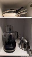 Food processor, hand mixer, and frying pans stored on shelves; shows all items in the lot