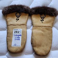 Pair of Indigenous leather mittens laid flat showing the tan leather and fur trim with beaded floral designs