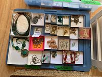 Overhead photo of assortment of necklaces and earrings in multiple small boxes on a tray and basket below containing more jewelry.