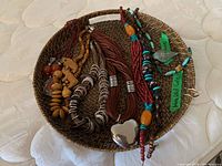 Wicker tray holding six necklaces with various beads and pendants.