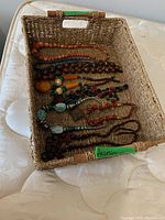 Wicker tray holding all necklaces visible inside, showing overall shape and contents