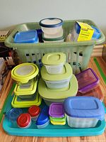 Top view of assorted plastic food storage containers with colorful lids piled in a green basket and blue tray