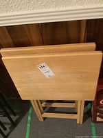 Two wooden folding TV tables shown from front view stacked together, showing light wood with wear.