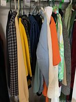 Photo showing a rack with assorted vintage ladies large size clothing including patterned and solid color suits, pants, and blouses.