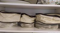 Three fabric zip-top storage containers on top shelf above stacked plates