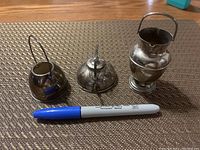Front view of the three sterling silver miniatures placed on textured surface with a blue marker for scale.