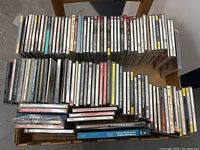 Photo showing a box filled with approximately 70 classical music CDs arranged side by side. The CDs are a mix of different classical works and artists.