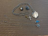 Seven pieces of silver-tone costume jewelry arranged on a textured surface, showing various necklaces with pendants and rings.