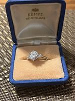 Ring shown inside blue jewelry box with cream-colored velvet insert and satin-lined lid showing 'Kemps The Jewellers'
