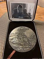 Medallion in open black presentation case showing reverse engraved 'White Pine 1937' and sculptor’s signature.