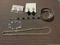 Top-down photo of six pieces of costume jewelry spread out on a textured brown surface. Includes two pairs of earrings, two bracelets, and one necklace.