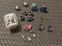 Photo showing various earrings including pearl studs, abalone teardrop clip-ons, pink butterfly studs, purple stone drops; also includes silver-tone rings and black beads.