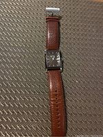 Full view of men's Fossil watch with rectangular stainless steel case and brown leather strap laid flat.