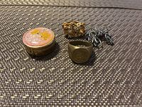 Pill box, two rings, and charm cluster displayed on fabric surface.
