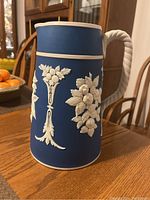 Side view of blue jug showing white floral relief decoration and twisted rope handle on the left side.