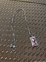 Full view of silver chain necklace with pendant on a textured brown surface.