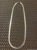 Silver box chain necklace laid out flat on a brown textured surface, showing the full length and clasp.