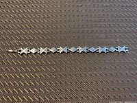 Full view of sterling silver bracelet showing alternating diamond-shaped and X-shaped links on textured surface background.