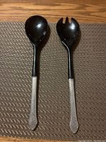 Pair of serving utensils with black heads and sterling silver floral engraved handles placed on a textured mat.