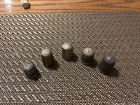Photo of 5 sterling silver thimbles with engraved and dimpled textures on woven mat surface.