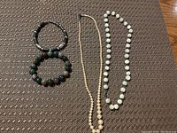 Four pieces of jewelry arranged on a brown textured fabric background: two beaded stretch bracelets and two bead necklaces.