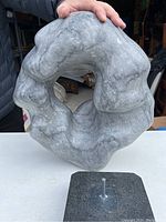 Full view of grey marble sculpture held above black stone base showing mounting peg