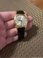 Front view of the vintage Chronosport wristwatch on hand, showing gold-tone case, silver dial with Arabic numerals and black leather strap