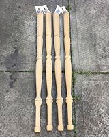 Four brand new wooden table legs placed vertically on outdoor ground, showing their full shape and length.