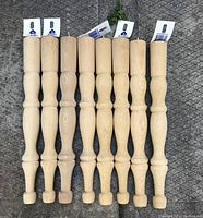 Photo showing all eight wooden table legs lined up, tag labels attached.