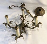 Antique brass chandelier with four arms, candle-style bulbs and hanging lower crystals, chain and wiring visible needing repair or rewiring.