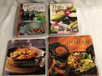 Top view of four cookbooks titled Twelve, Thai & South-East Asian Cooking, Contorni, and Classic Indian.