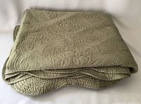 Folded large sage green quilted blanket showing overall color and thickness
