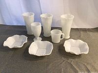 Photo showing all eight milk glass pieces including vases, goblet, mug, and bowls arranged on fabric surface